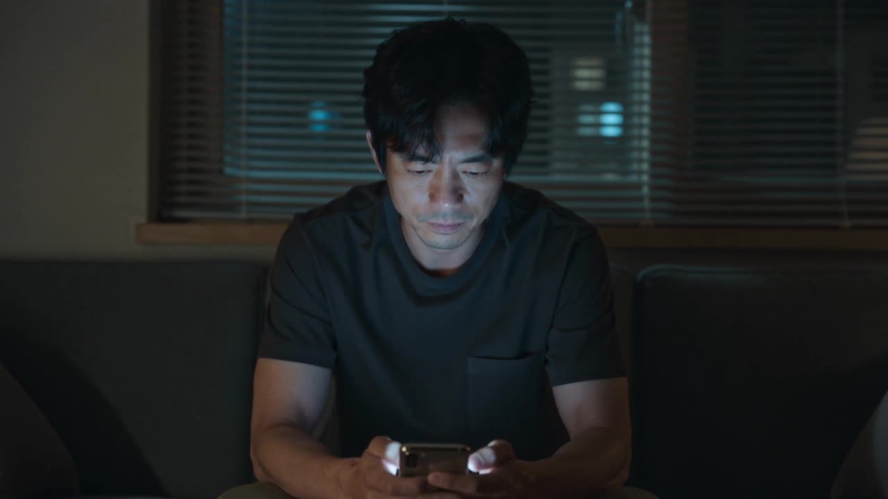 A man at a kitchen table late at night, lit by his phone.